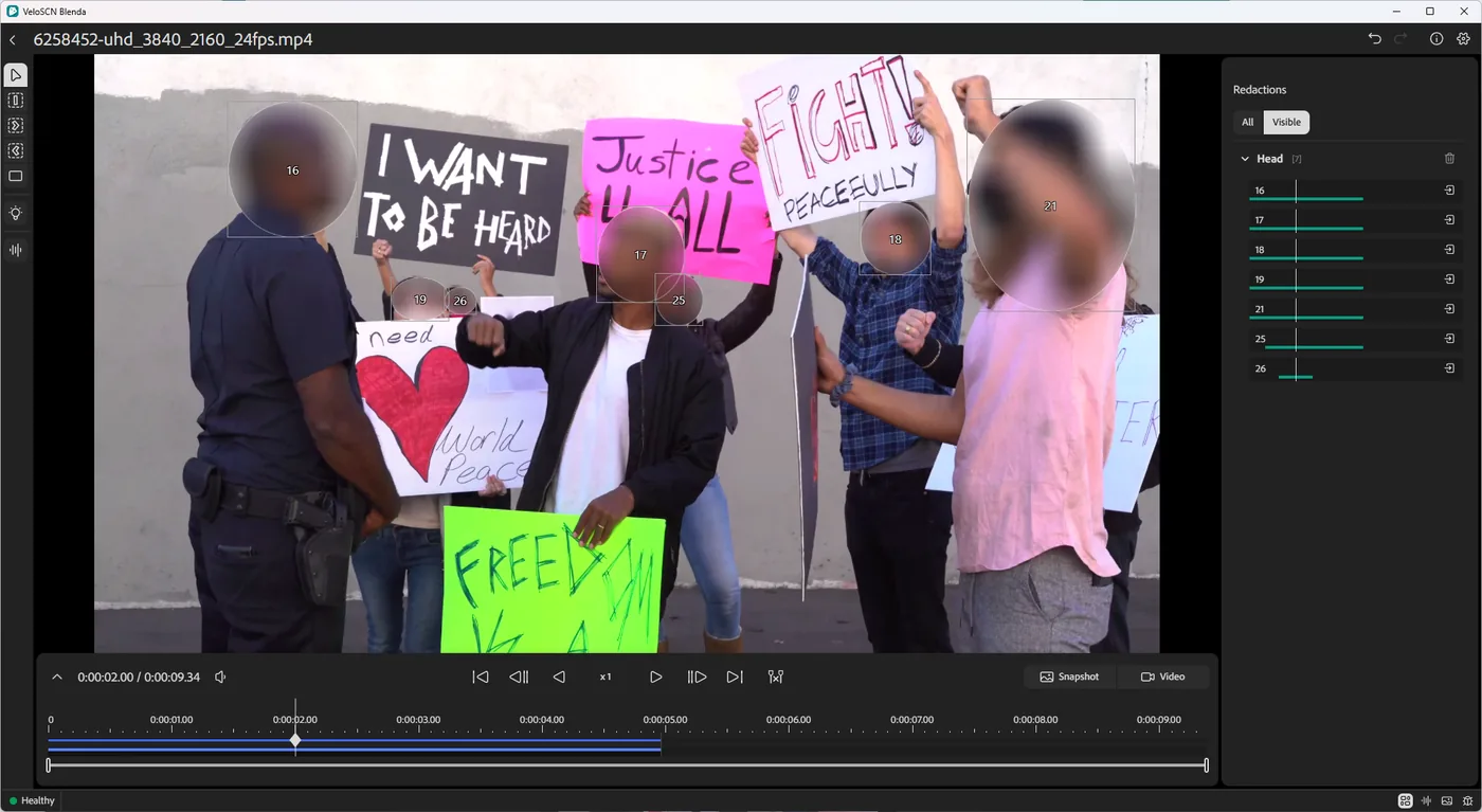 The same clip with every head automatically detected and blurred, each tracked across the timeline in the Redactions panel